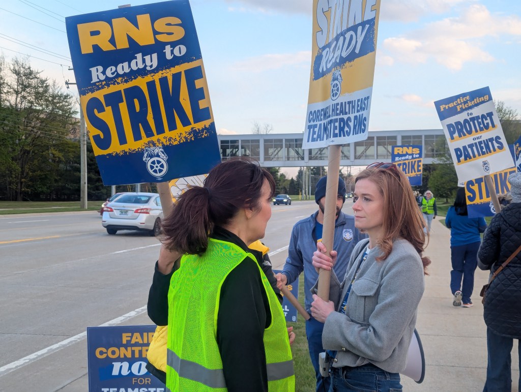 Mallory McMorrow talks with people holding signs.