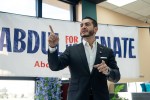 Abdul El-Sayed speaks at a campaign event in front of a campaign banner, gesturing toward the audience while addressing supporters indoors.