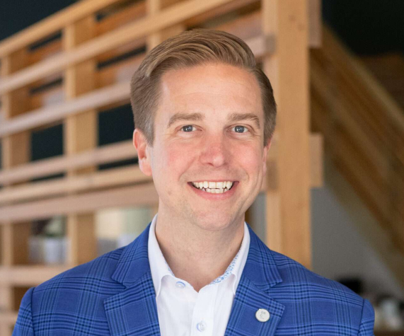 headshot of a man standing in front of a wooden beam structure