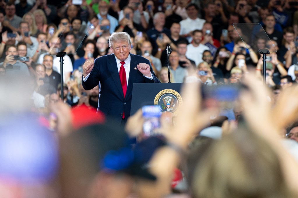 Donald Trump smiling on a stage. Supporters are cheering him on. 