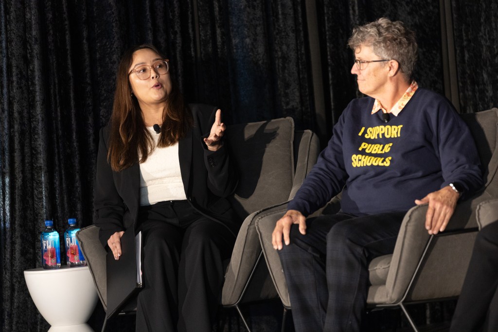 Two people talk while seated on a stage