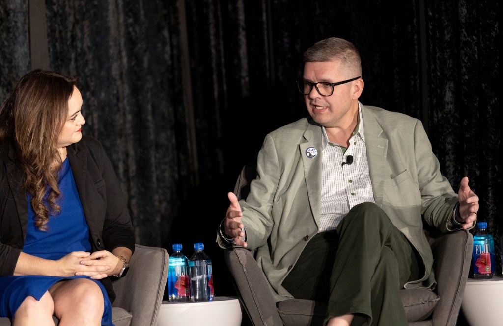 Two people talk while seated on a stage